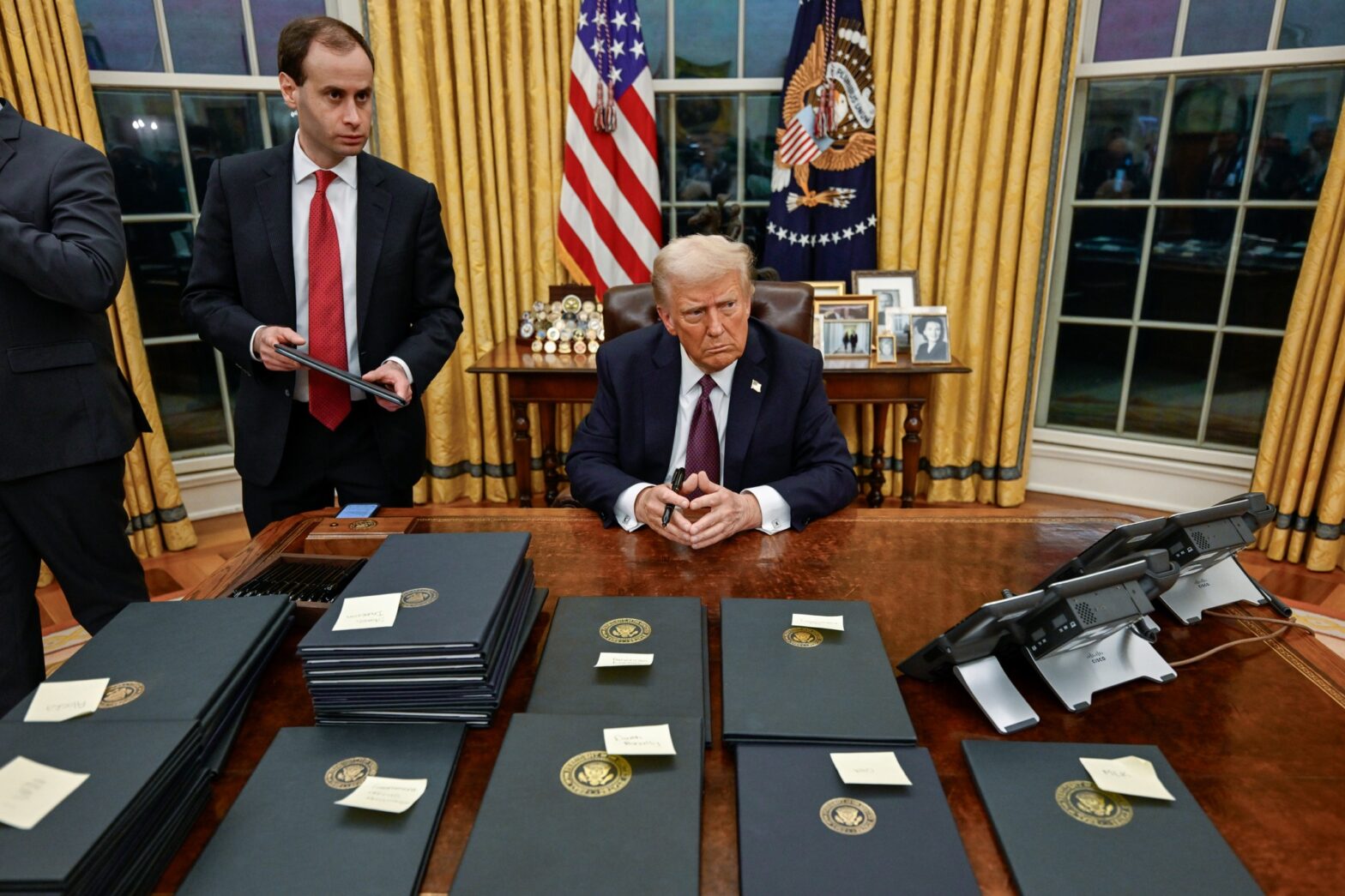 Donald Trump sitzt an seinem Schreibtisch. Hinter ihm hängt die amerikanische Flagge.