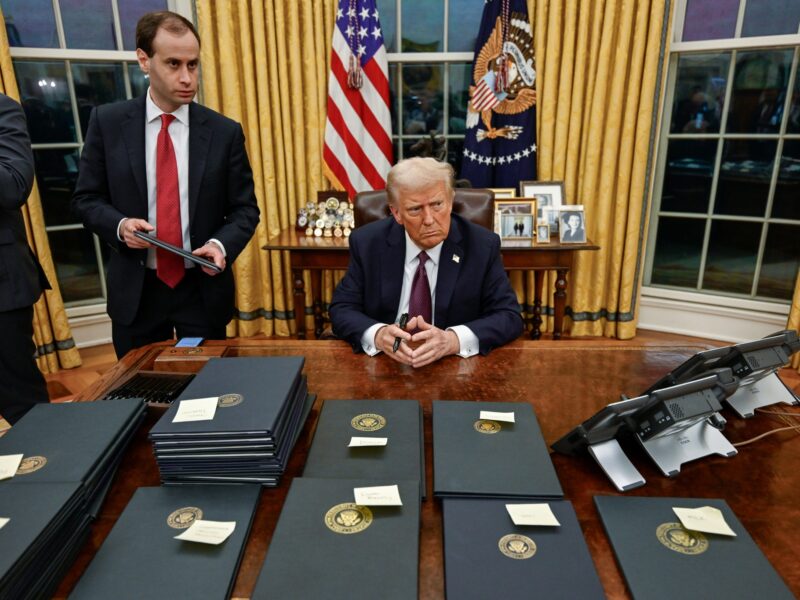 Donald Trump sitzt an seinem Schreibtisch. Hinter ihm hängt die amerikanische Flagge.