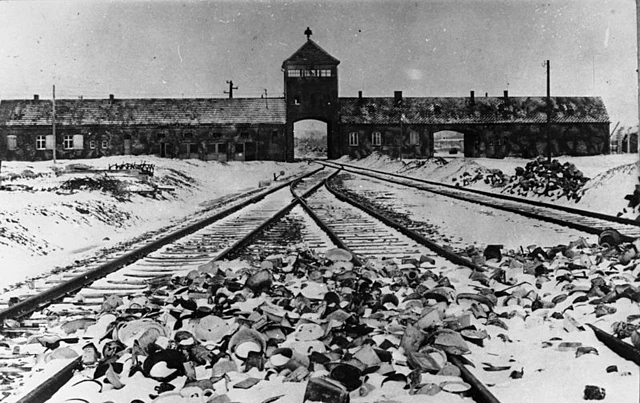 KZ Auschwitz, Einfahrt Polen 1945 nach der Befreiung, im Vordergrund von den Wachmannschaften zurückgelassene Ausrüstungsgegenstände.