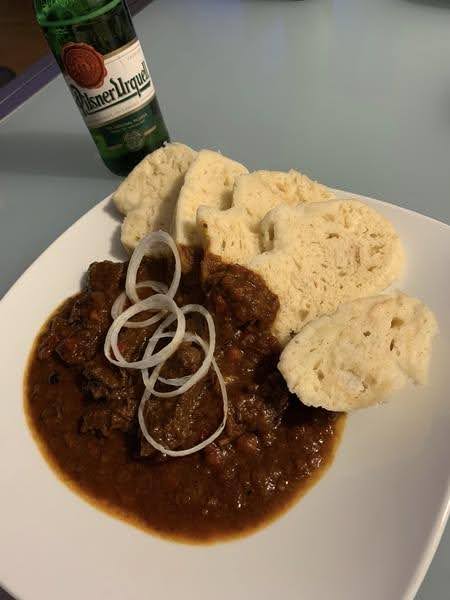 Eine Flasche Bier neben einem weißen Teller mit böhmischen Gulasch serviert mit Knödeln.