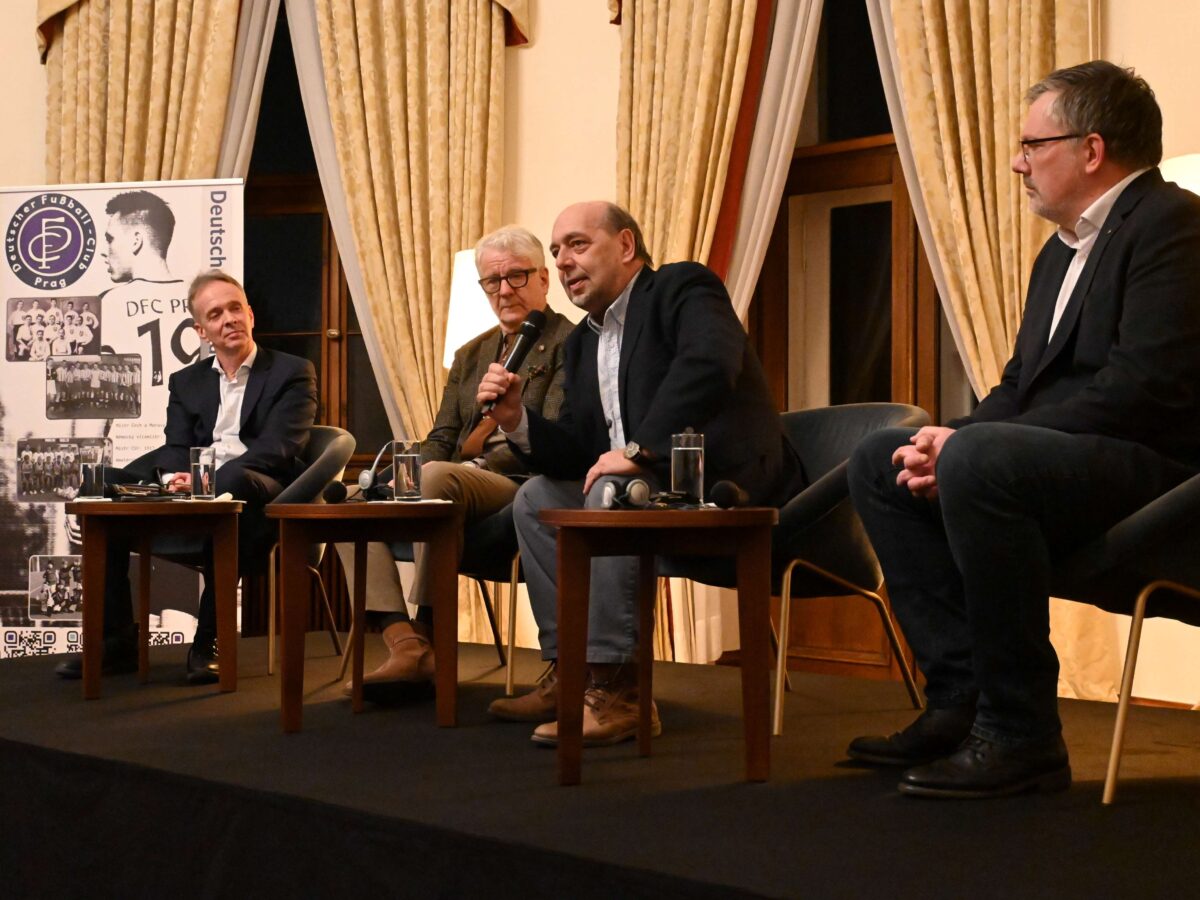 Martin Holler, Marcel Reif, Tomáš Kraus und Filip Bláha sitzen nebeneinander auf Stühlen im Kuppelsaal der deutschen Botschaft in Prag.