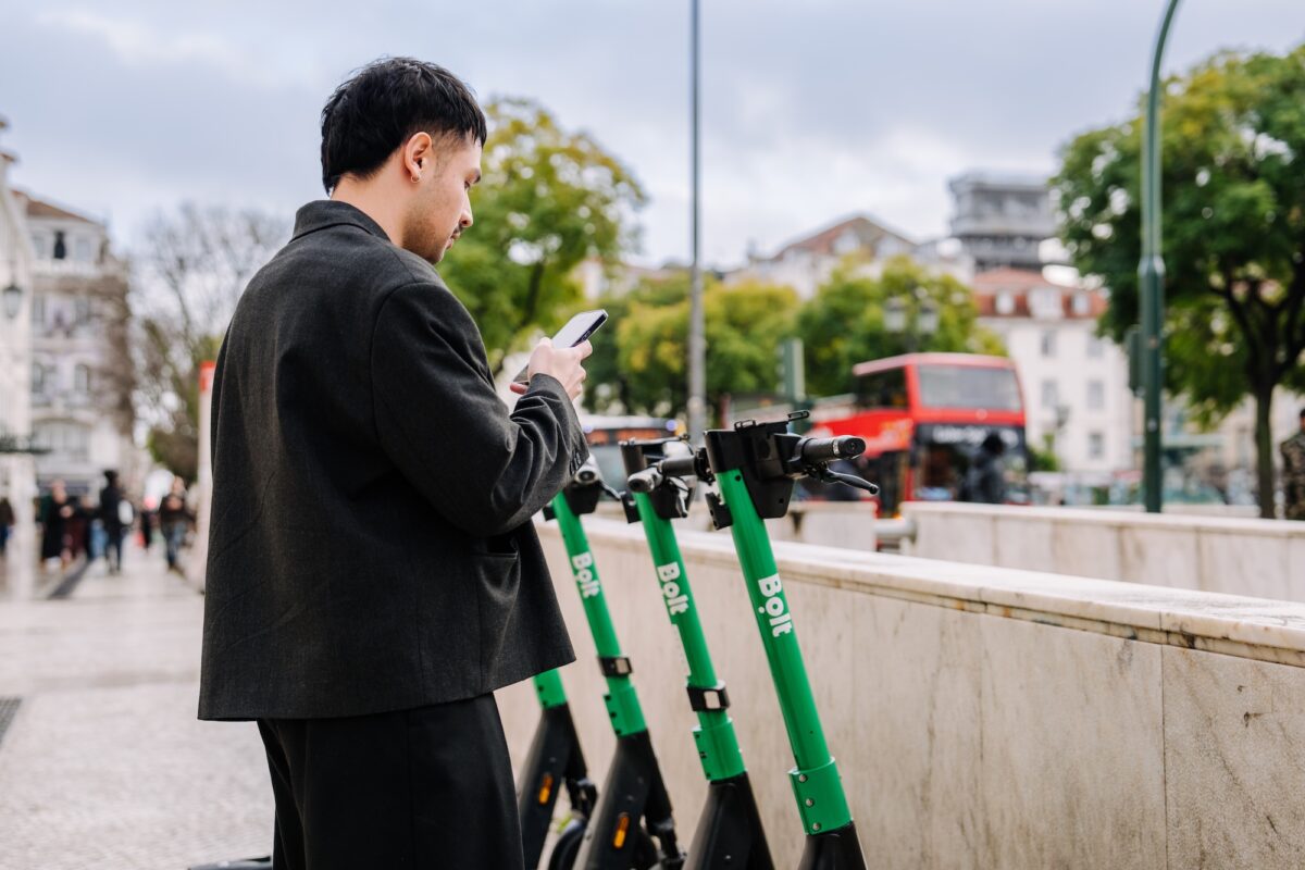 Ein Mann steht mit seinem Smartphone vor mehreren Leih-E-Scootern in Prag – aufgenommen aus größerer Distanz, als Titelbild für einen Artikel über das mögliche Aus der E-Scooter in der Stadt.