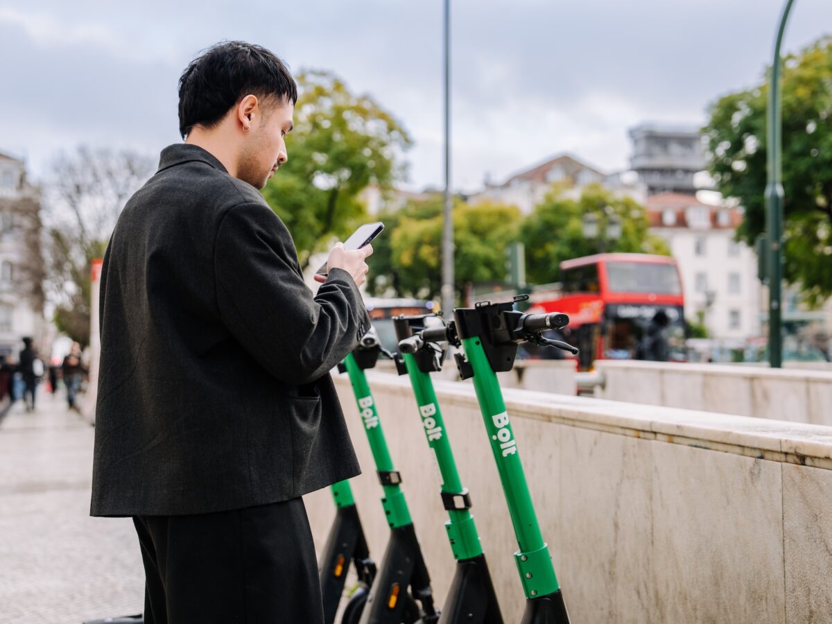 Ein Mann steht mit seinem Smartphone vor mehreren Leih-E-Scootern in Prag – aufgenommen aus größerer Distanz, als Titelbild für einen Artikel über das mögliche Aus der E-Scooter in der Stadt.