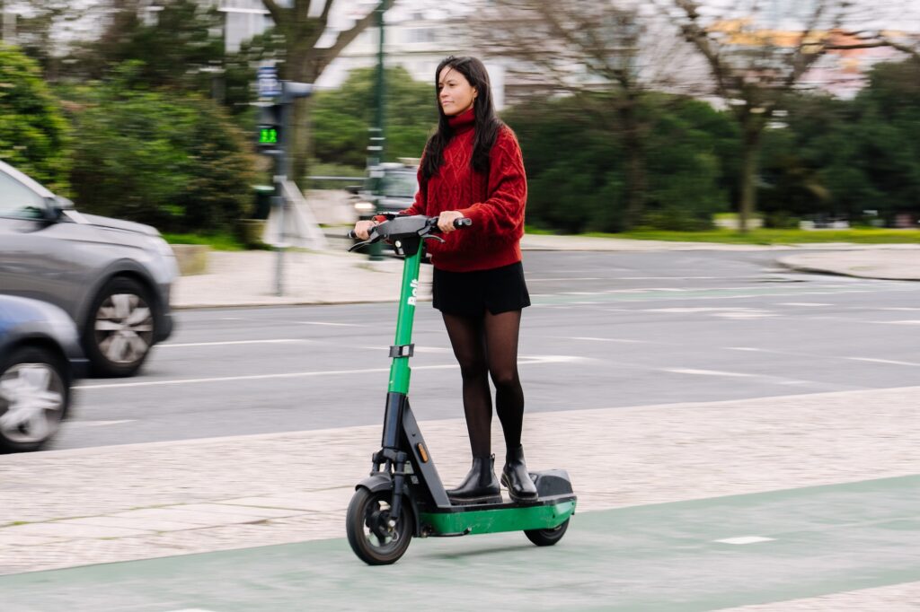 Eine Frau fährt auf einem E-Scooter eine Straße entlang, im Hintergrund Prager Stadtarchitektur. Das Bild steht im Zusammenhang mit einem Artikel über das mögliche Aus von Leih-Scootern in Prag.