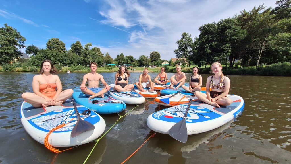 Jugendliche machen SUP-Yoga auf Stand-Up-Paddle-Boards beim deutsch-tschechischen Sommercamp 2025 am Perlsee in Waldmünchen.