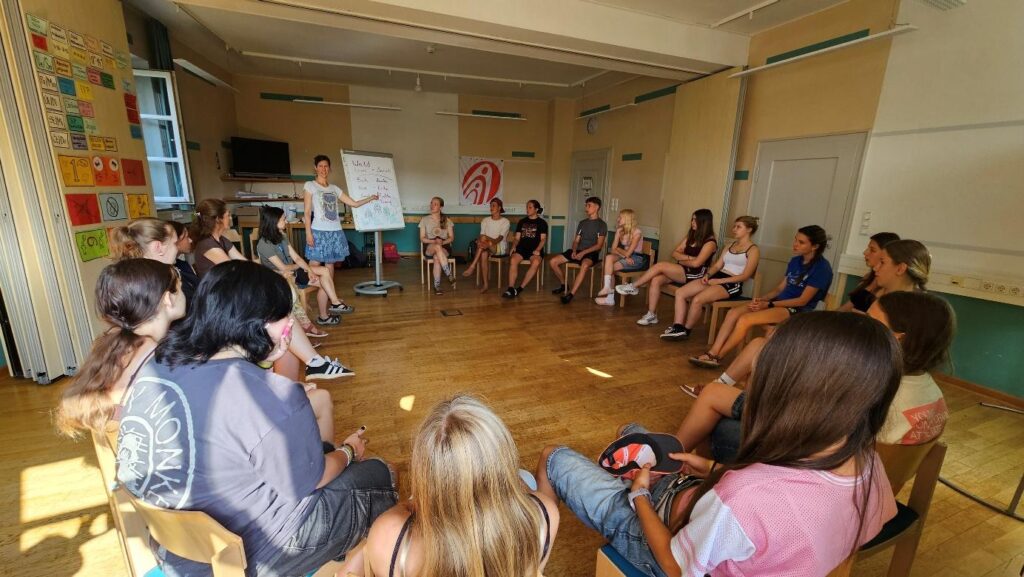 Jugendliche sitzen im Stuhlkreis während eines Workshops beim deutsch-tschechischen Sommercamp 2025 in Waldmünchen.