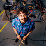 Musiker Jonas Holland alias AfterCooking steht vor seinem Setup aus Rohren und Töpfen in verschiedensten Größen.