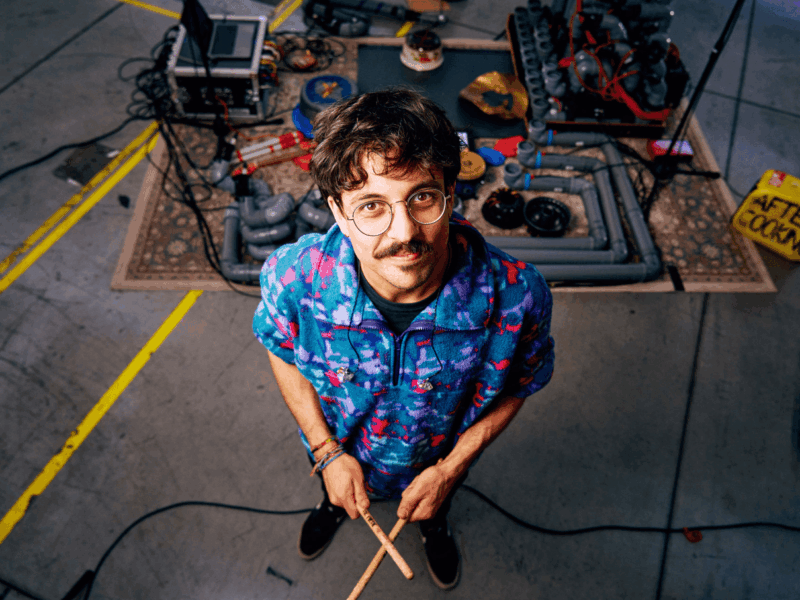 Musiker Jonas Holland alias AfterCooking steht vor seinem Setup aus Rohren und Töpfen in verschiedensten Größen.