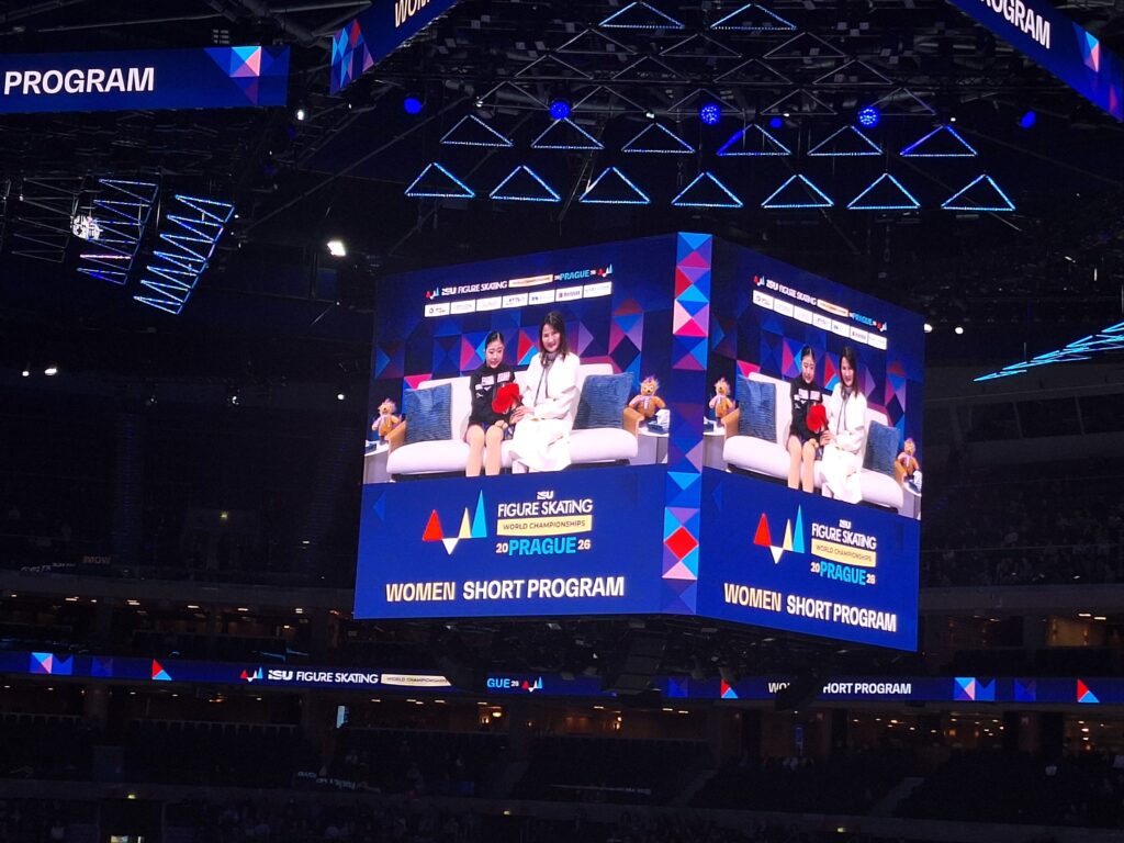 Der Bildschirm überträgt die Couch, auf der die Eiskunstläuferinnen ihre Bewertung, für das Kurzprogramm der Eiskunstlauf-Weltmeisterschaft 2026, erfahren.